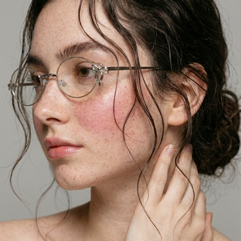A beautiful young woman with freckles looking gracefully featuring Y2K retro oval eyeglasses in silver metal for everyday makeup-free wear.